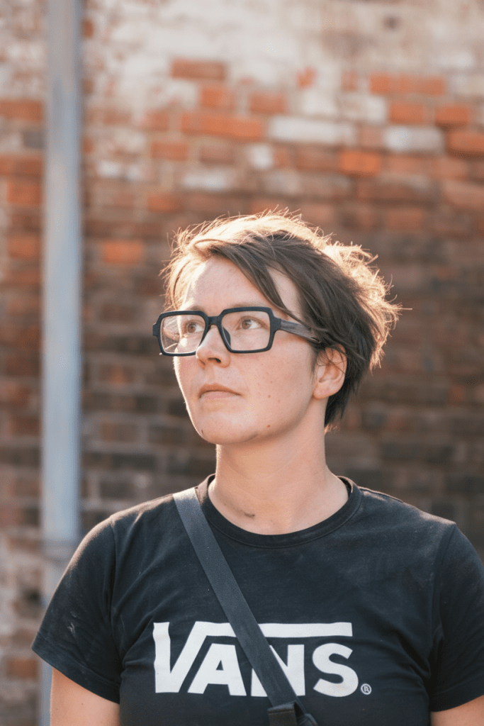 A close-up, portrait-oriented crop of the existing photo of the maker in the workshop, zoomed so the composition tightly frames from just below the collarbone to above the head, excluding the shirt print while keeping natural lighting and realistic detail.